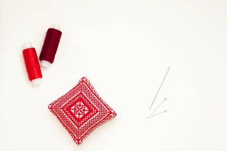 Flat lay with handmade red embroidered needle pad, thread spools, pins, needles, mock up, top view. Layout mockup on blank white background for needlework, sewing poster, banner. Empty space for text.の写真素材