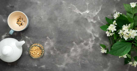 White tea pot, herbal dry tea, jasmin blossom, cup, black white marble background flat lay. Tea time top view template long web banner. Copy space mockup design. Floral spring flowers cafe conceptの写真素材