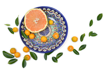 Cut grapefruit and citrons on old vintage painted plate on a white background with scattered leavesの写真素材