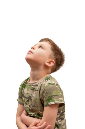 A boy in a camouflage t shirt on a white background with his arms crossed looks up with sadnessの写真素材