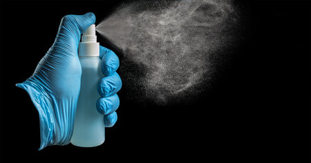 A gloved hand sprays sanitizer  a black background. Medical background. Take care. Stay at home. . Place for text.  pathasの写真素材
