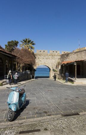 View of the sea through one of the city gates in the old town of Rhodes, Greece, with a motor scooter in the foregroundの写真素材