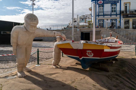 Stone statues of a man and boy next to a wooden boat in Albufeira, Algarve, Portugalのeditorial素材