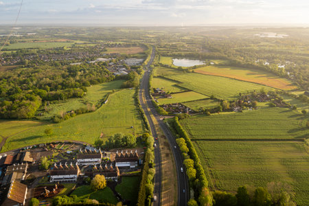 Aerial view of the A228 road cuttiing through fields in the Kent countryside with rows of Oast Houses in the bottom corner, in Kent, UKの写真素材