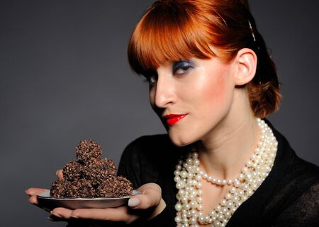 Beautiful retro woman with red lips holding many truffel shocolate sweets. focus on sweetsの写真素材