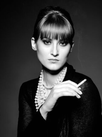 Beautiful retro woman with red lips holding cigarette and smoking. black and white pictureの写真素材