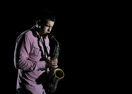 Young handsome man playing music on saxophone. black backgroundの写真素材
