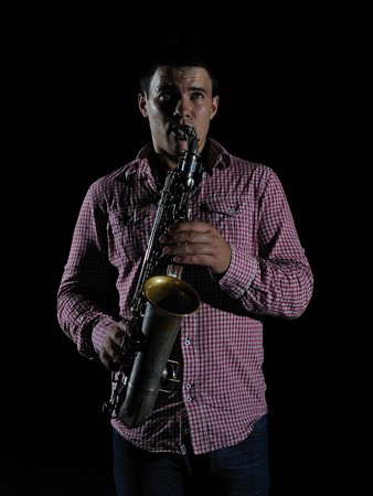 Young handsome man playing music on saxophone. black backgroundの写真素材