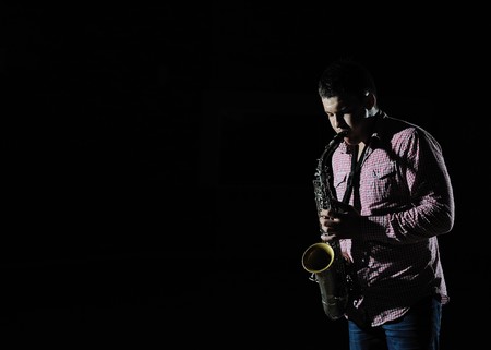 Young handsome man playing music on saxophone. black backgroundの写真素材