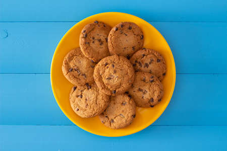 Chocolate chip cookies on a yellow plate over ocean blue wooden table