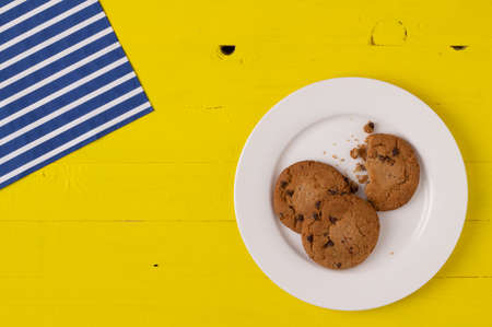 Chocolate chip cookies on a white porcelain plate over yellow wooden tableの写真素材