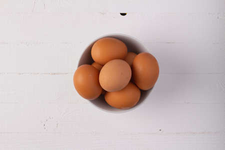 Organic eggs in a white bowl over white wooden table