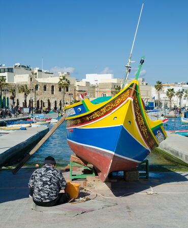 MARSAXLOKK, MALTA. 30th December 2019. A fisherman freshens up the painted eyes of Osiris on the prow of his Maltese 'Luzzu' - one of the brightly-coloured traditional fishing boats still used today in villages such as Marsaxlokk.のeditorial素材