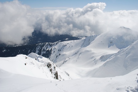A mountain winter slope in clouds in a landscape with white snow.
