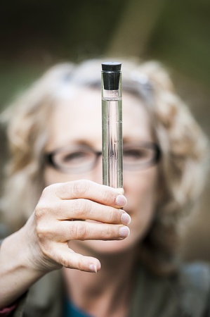 A female ecologist gathers water samples from a natural stream, surrounded by river rocks and natural geological formationsの写真素材
