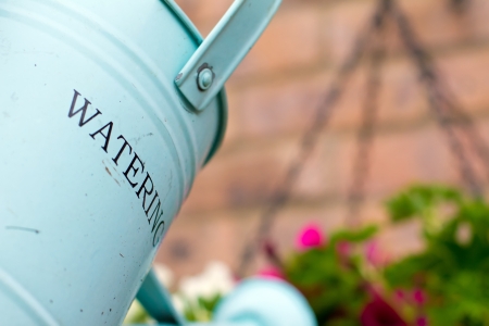 green metal watering can over a hanging basketの写真素材