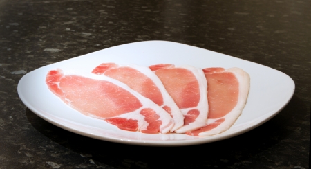uncooked rashers of bacon on a white plateの写真素材