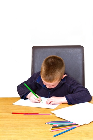 young boy drawing with pencils on a tableの写真素材