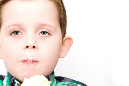 handsome little boy eating a fresh cream cup cake with messy faceの写真素材