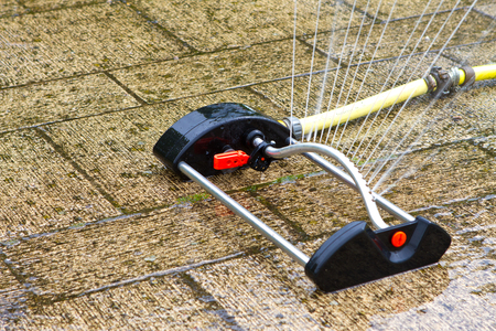 sprinkler watering the lawn and garden on a hot summers dayの写真素材