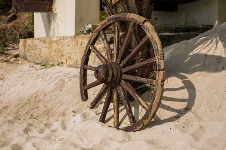 Old brown wooden wheel on sand beach の写真素材