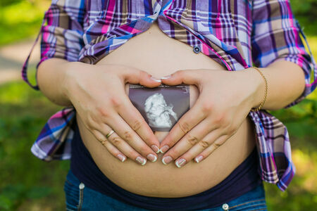 Happy pregnant woman in park making heart sign on bellyの写真素材