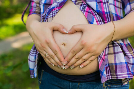 Happy pregnant woman in park making heart sign on bellyの写真素材