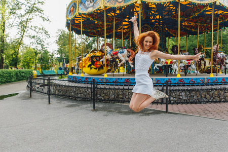 Beautiful red hair girl jumps near the carousel with hoursesの写真素材