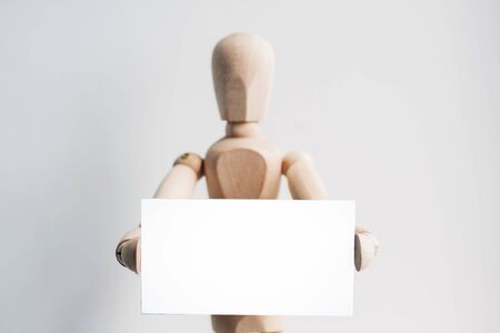 Wooden mannequin holding a business card. Isolated white backgroundの写真素材