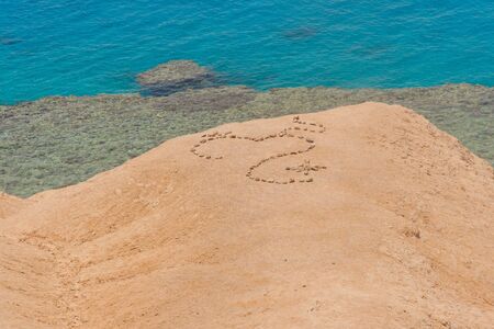 Love heart shape on sand made of stones, symbol of love on the background of the blue sea.の写真素材