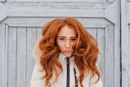 Portrait of a beautiful red hair young woman in warm clothes outdoor on the grey wooden background....