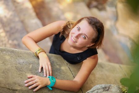 Outdoor summer portrait of young beautiful girl with blond hair posing in short black stylish dress standing on the stairs.の写真素材
