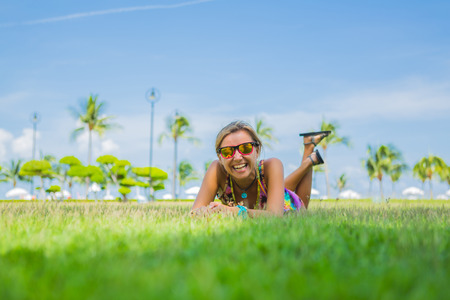 Outdoor portrait of young woman lying on the grass with palm trees on the background..の写真素材