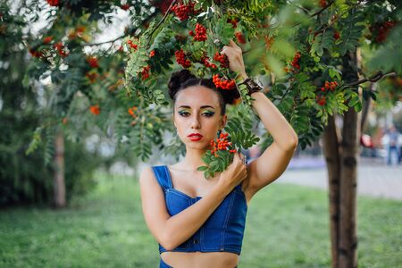 Beautiful young woman with bright make up under the rowan tree with rowan berries.の写真素材