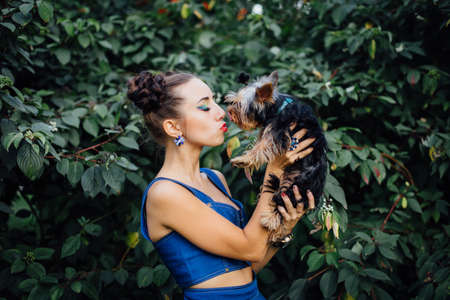 Young beautiful woman kisses Yorkshire Terrier near green bushの写真素材