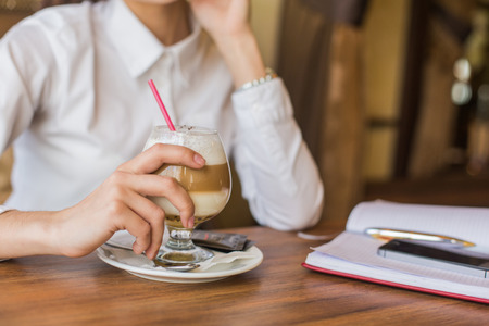 Brunette woman in business clothes sitting at the cafe drinking latte coffee.の写真素材