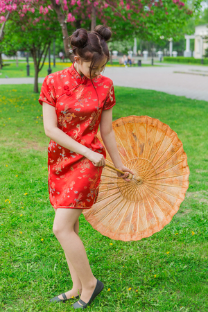 Beautiful asian girl in traditional chinese red dress with bamboo umbrella near pink apple tree in the park.の写真素材