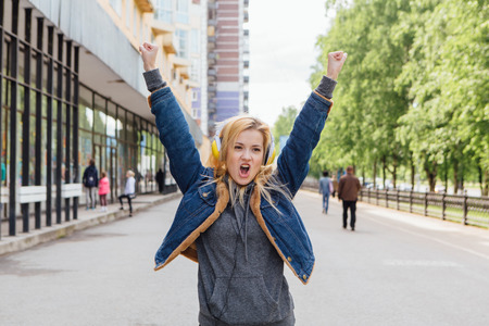 Girl listening to music streaming with headphones and dancing on the street.の写真素材