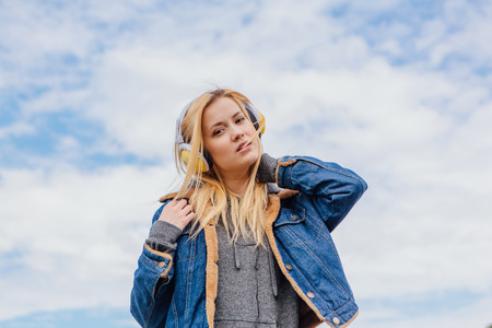 Girl listening to music streaming with headphones and dancing on sky backgroundの写真素材