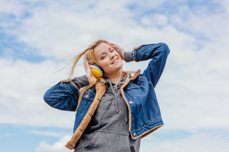 Girl listening to music streaming with headphones and dancing on sky backgroundの写真素材