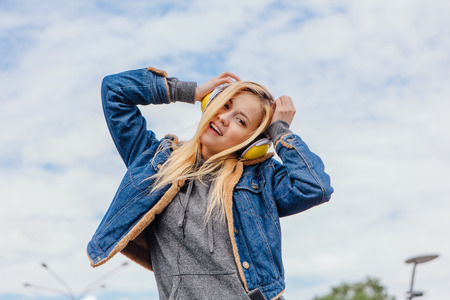 Girl listening to music streaming with headphones and dancing on sky backgroundの写真素材
