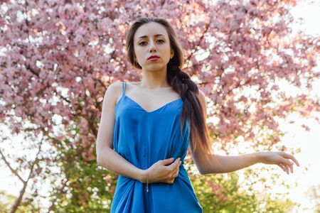 Beautiful young woman dressed in blue overalls standing near the blooming pink apple tree.の写真素材