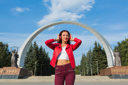 Girl in red jacket listening to music streaming with headphones and dancing on the street.の写真素材