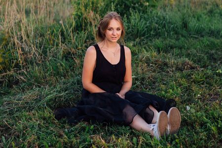 Slim blonde girl with make up in black long dress in the field at sunsetの写真素材