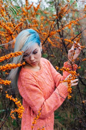 Portrait of a young woman with blue hair in a bush of sea-buckthornの写真素材