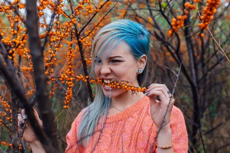 Portrait of a young woman with blue hair with a branch of sea-buckthorn in teethの写真素材