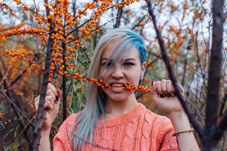 Portrait of a young woman with blue hair with a branch of sea-buckthorn in teethの写真素材