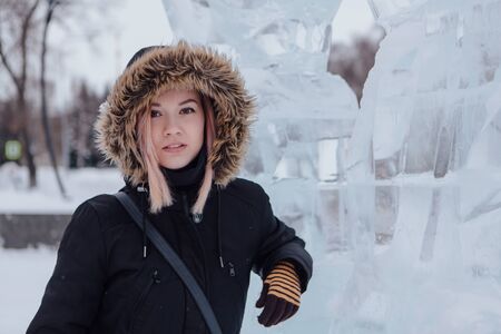 Winter fashion. Portrait of a beautiful young woman in warm clothes outdoor near the ice sculpture.の写真素材
