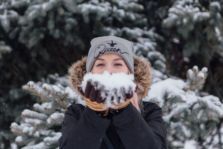 Winter fashion. Portrait of a beautiful young woman in warm clothes outdoor blowing on snow in handsの写真素材