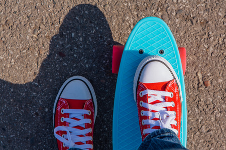 Close up of feet of a girl in red sneakers rides on blue penny skate board with pink wheels. Urban scene, city life. Sport, fitness lifestyle.の写真素材